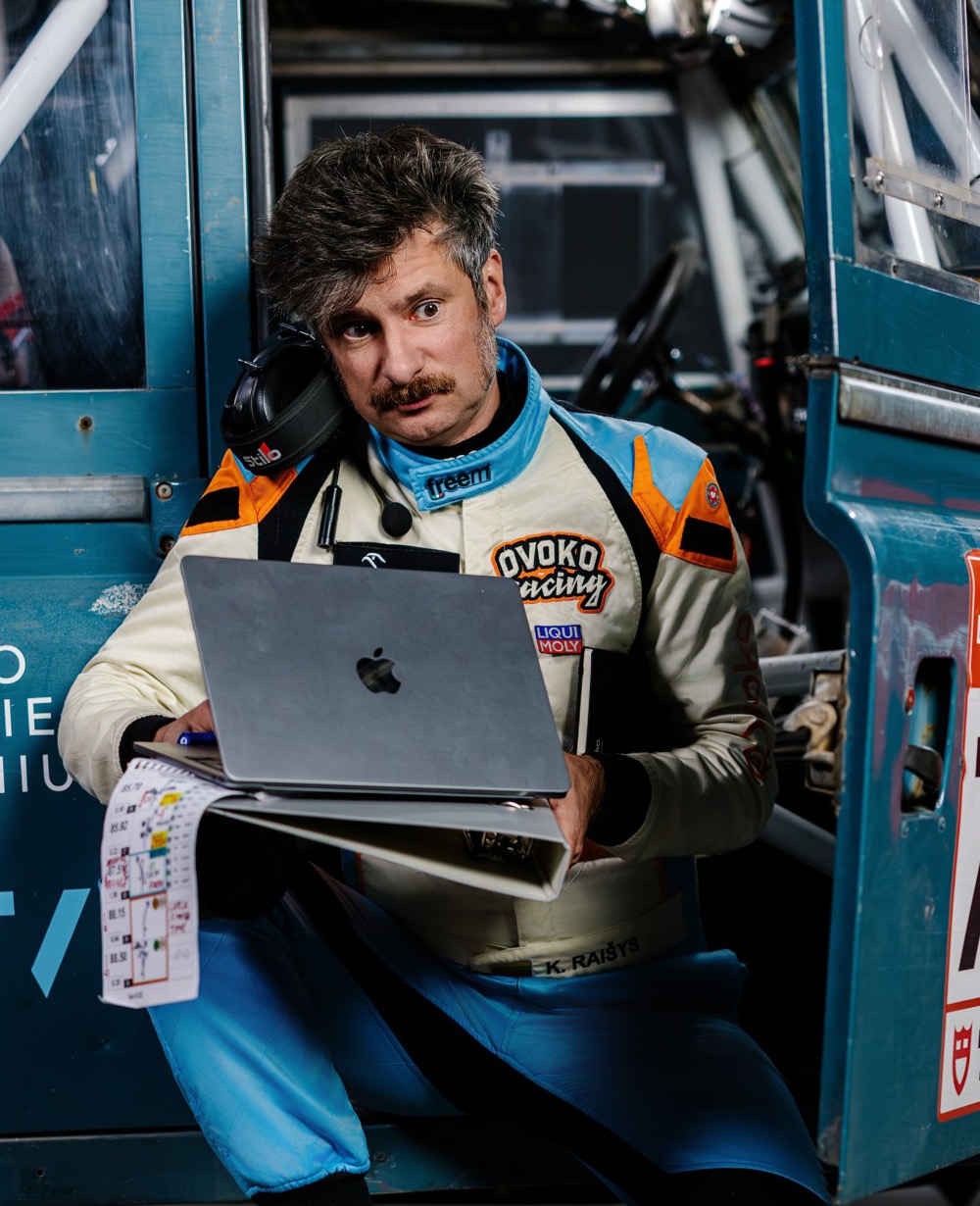 Karolis Raišys with a laptop and a roadbook, sitting by his rally car